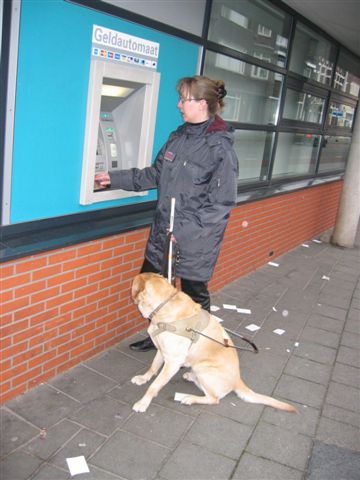 Kim met geleidehond bij pinautomaat